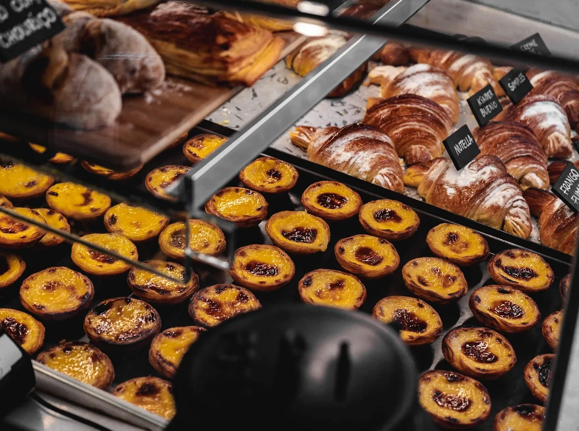 Bakker med pastel de nata og croissanter bag glasset i en bagerdisk i Lissabon, håndskrevne skilte over dem